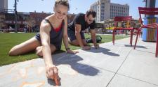 This image shows a woman and a man sitting on turf while drawing sea creatures with chalk on the nearby cement.