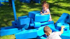 Toddler playing with large blue foam stacking blocks in island park 