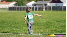 kid in grass field with participant number bib on throwing a frisbee