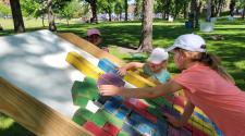three hids in hats and painted faces playing large scale colorful tetris in island park 