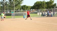 Male swinging softball bat on softball field with catcher standing behind.  Teammates and spectators in the background
