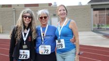 Three women wearing medals smile together on a track after competing in the North Dakota Senior Games.