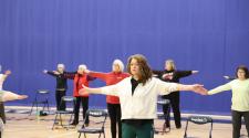 adults 55+ standing in gym with chair next to each stretching for the SAIL program