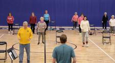 adults 55+ standing in gym with chair next to each stretching for the SAIL program