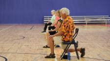 adults 55+ sitting in gym on a chair stretching for the SAIL program
