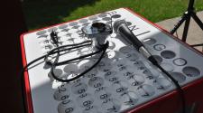 A bingo cage and microphone rest on top of a numbered bingo board during an outdoor event.